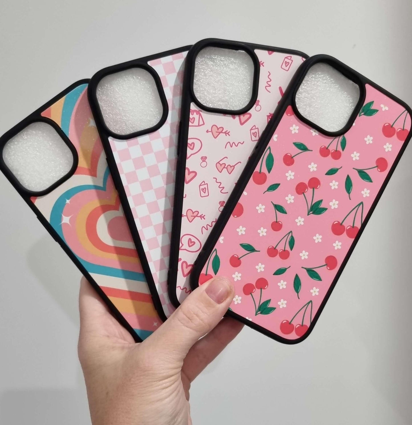 Colorful iPhone 15 cases with unique designs including hearts, checkered pattern, and cherries, offering stylish and shock-proof protection.